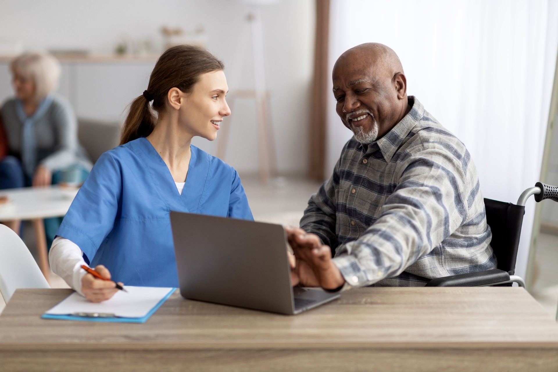 Friendly nurse assisting senior black patient using laptop